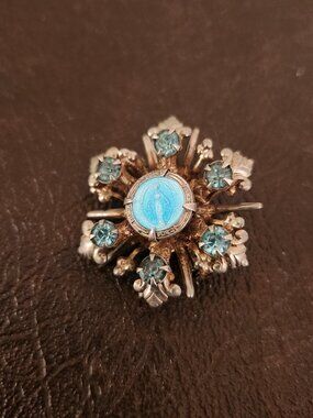 Vintage brooch features an Immaculate Conception design with blue rhinestones